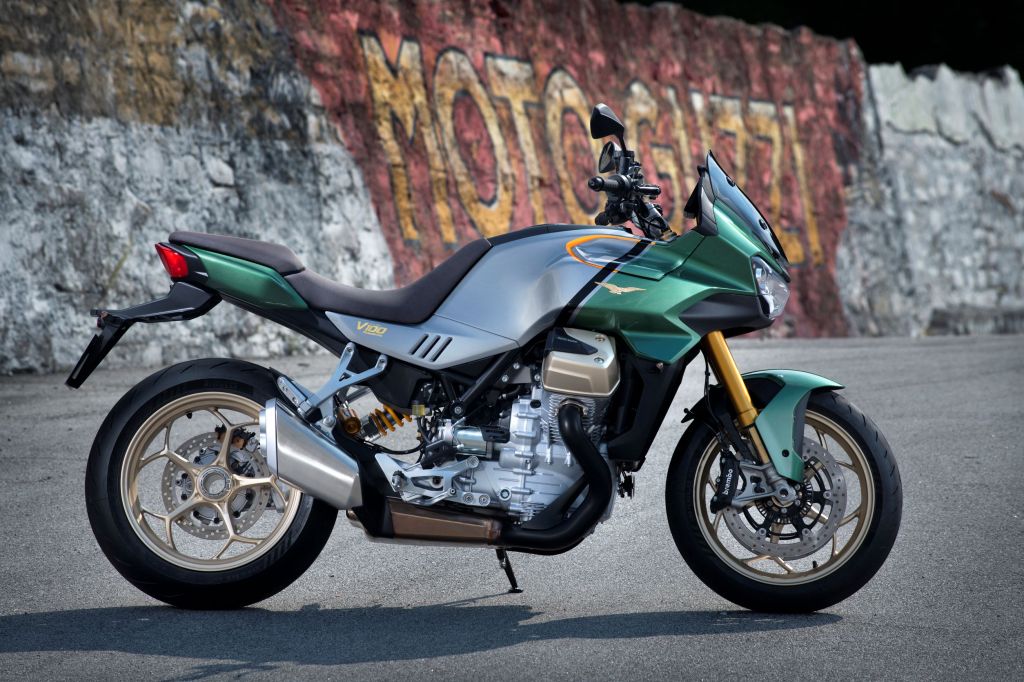 The side view of a green-and-silver Moto Guzzi V100 Mandello by a graffiti-covered brick wall