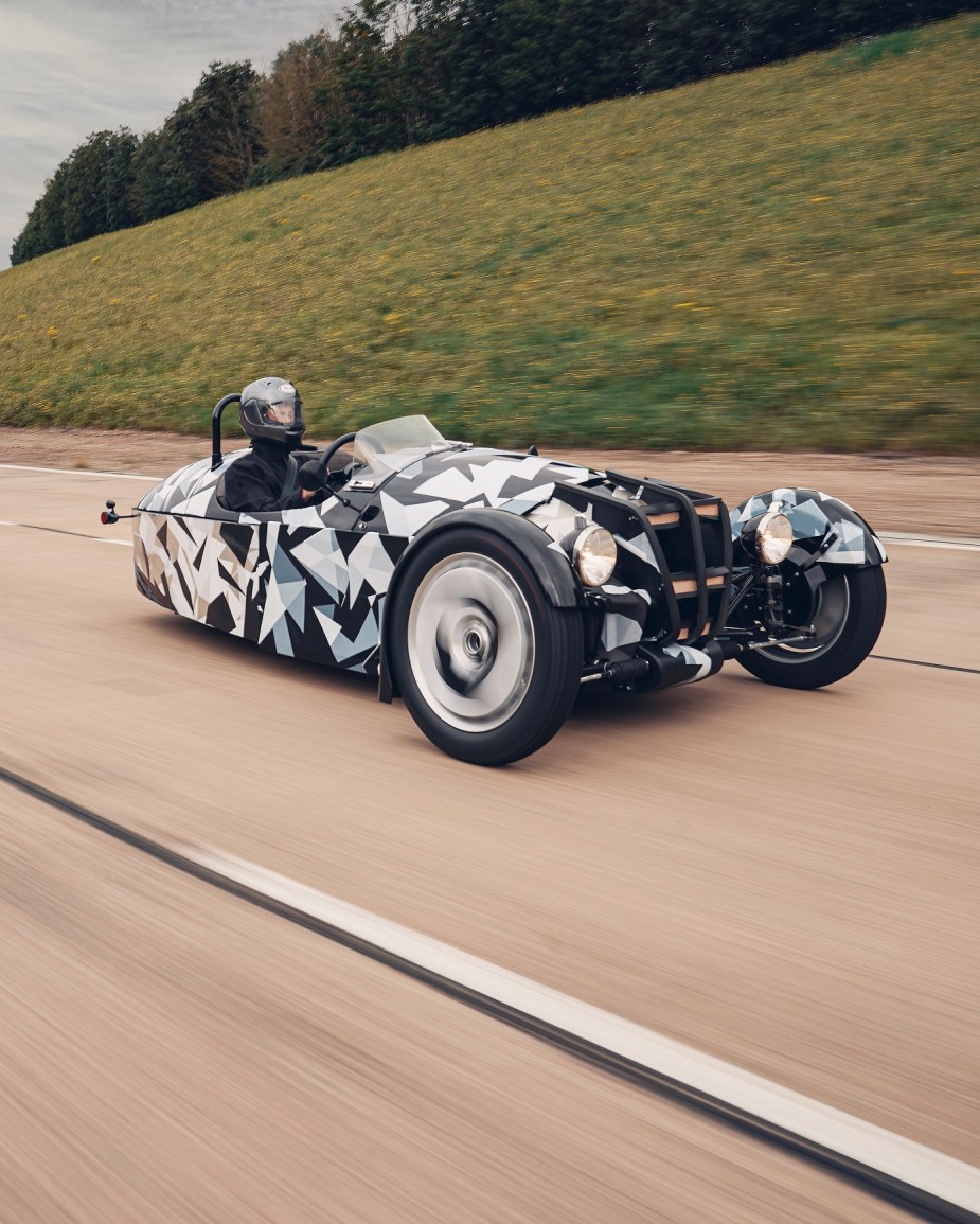 A black-white-and-gray camouflaged new Morgan 3-Wheeler testing on a highway