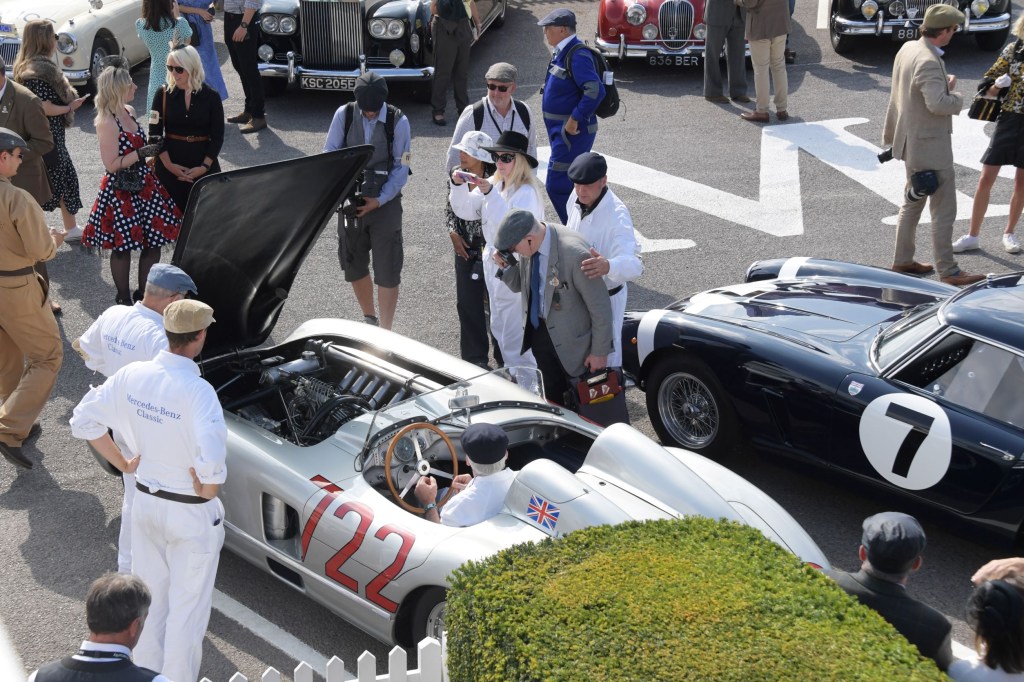 Onlookers in vintage clothing look at classic cars at the 2021 Goodwood Revival, including Sir Stirling Moss's silver No. 722 1955 Mercedes-Benz 300 SLR