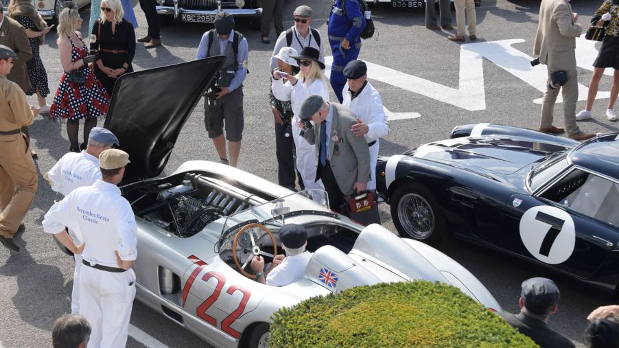 Onlookers in vintage clothing look at classic cars at the 2021 Goodwood Revival, including Sir Stirling Moss's silver No. 722 1955 Mercedes-Benz 300 SLR