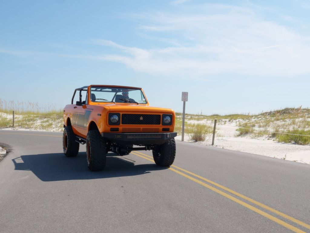 Orange and black 1979 International Harvester Scout driving by sand dunes