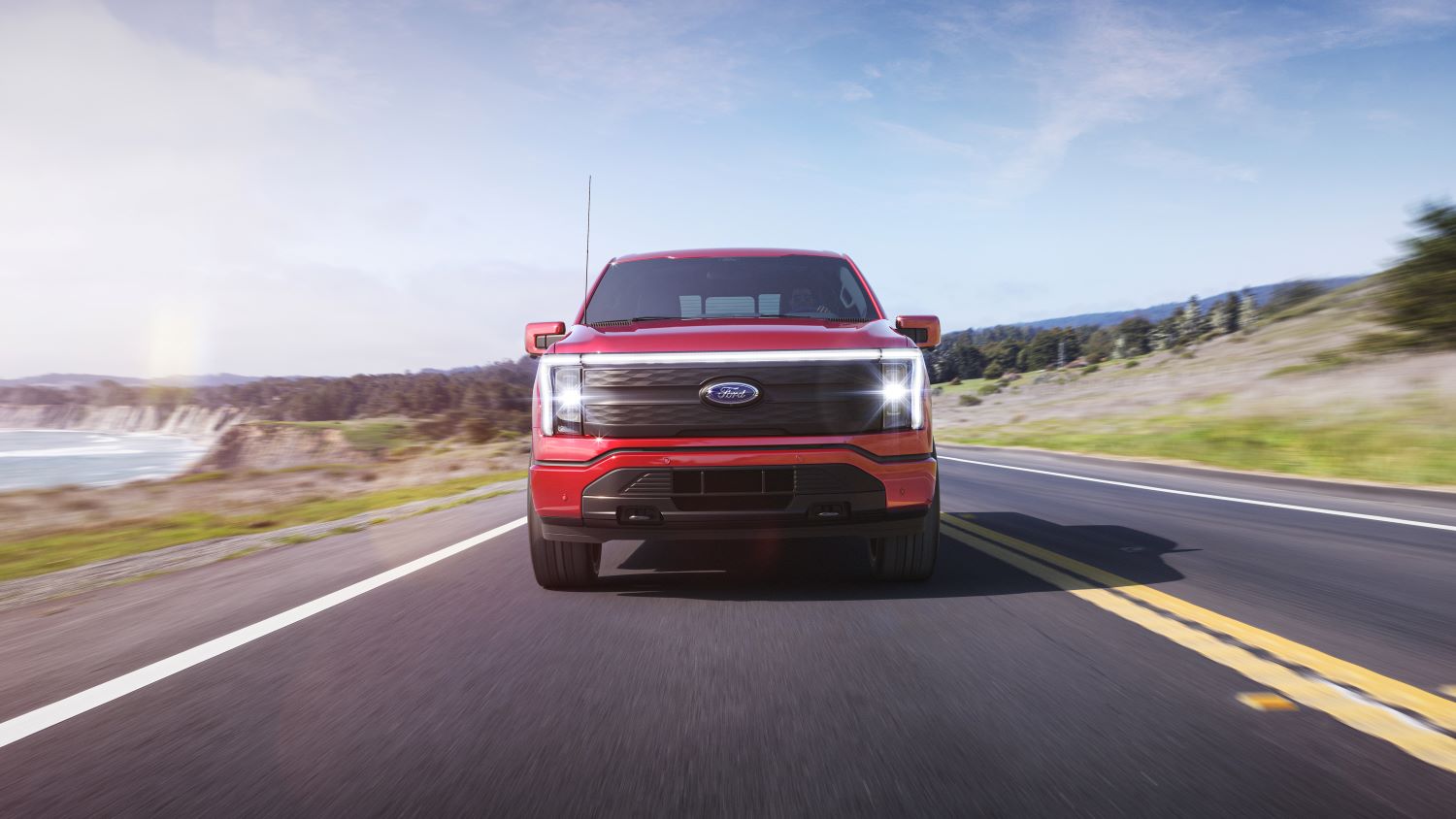 Red 2022 Ford F-150 Lightning driving on a coastal road