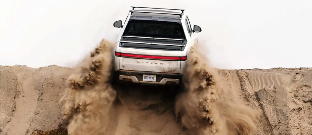 A white 2022 Rivian R1T climbing up a dirt hill.