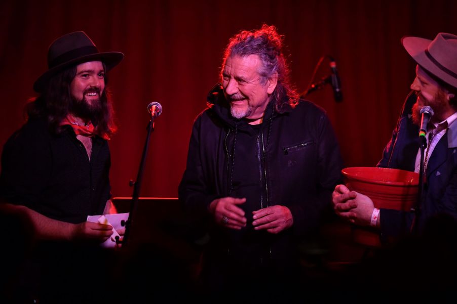 Robert Plant dressed in black on stage with a red curtain in the background.