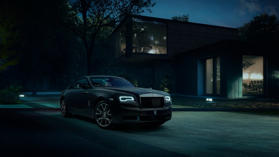A dark-colored Rolls-Royce Wraith Kryptos parked in front of a modern house at night
