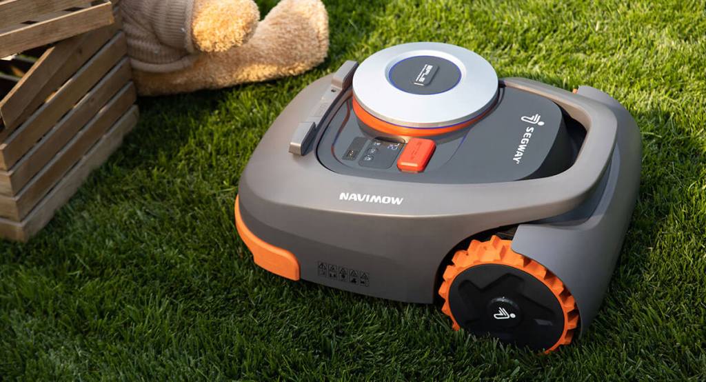 A segway navimow sits in a lawn area next to a wooden box and teddy bear