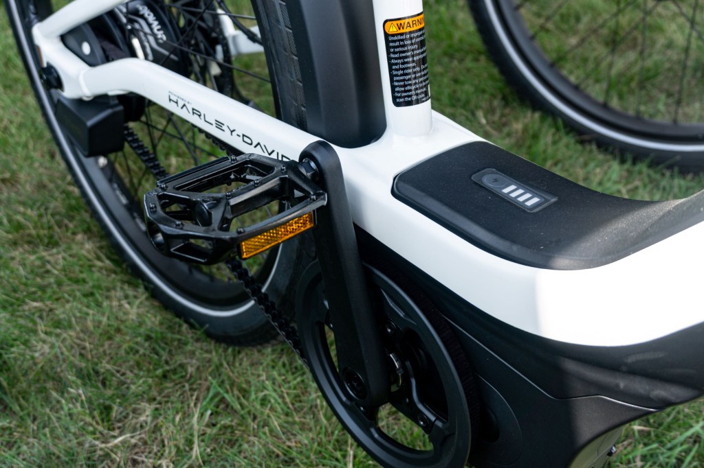 A close-up view of a black-and-white Serial 1 RUSH/CTY Step-Thru ebike's pedals, battery, and motor