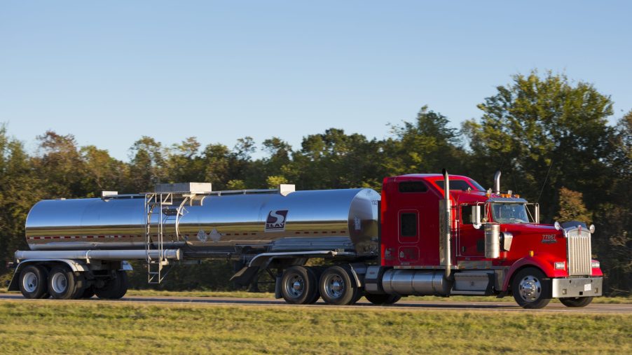 A red semi truck drives down the highway hauling an oil tanker