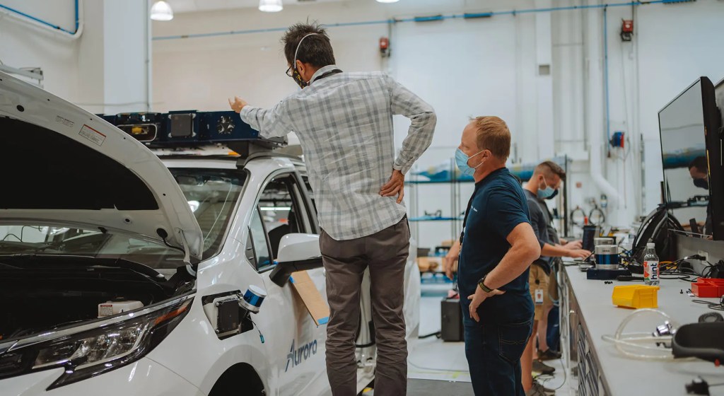 Technicians working on a white Aurora Toyota Sienna self-driving taxi