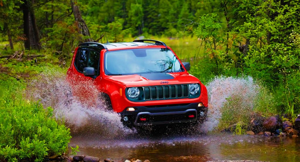 A red 2021 Jeep Renegade Trailhawk off-road SUV is driving through a shallow body of water.