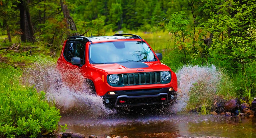A red 2021 Jeep Renegade Trailhawk off-road SUV is driving through a shallow body of water. 