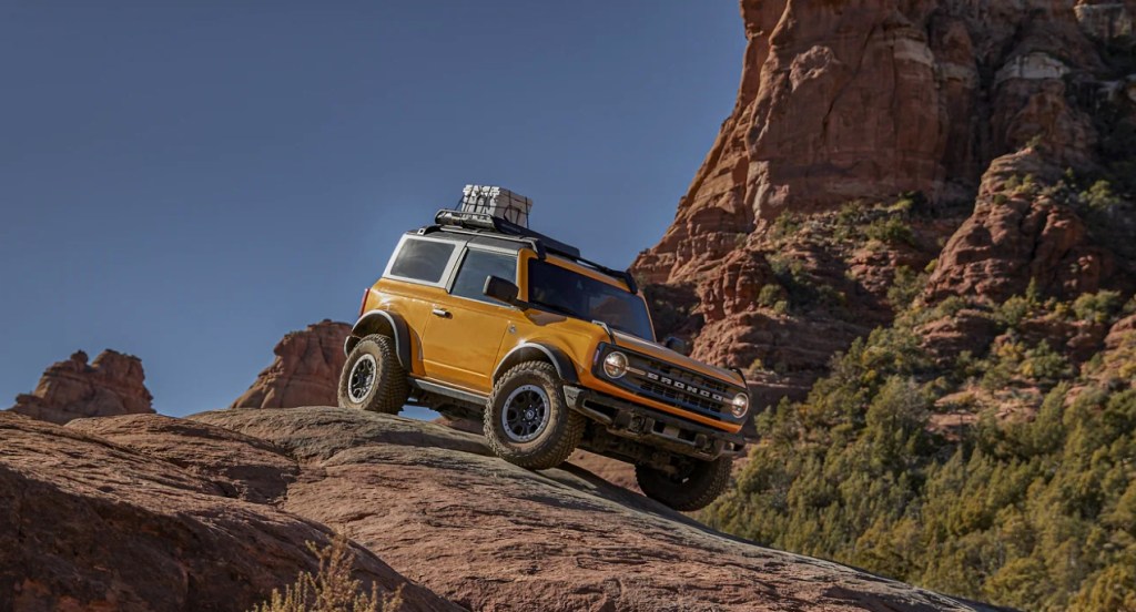 A yellow Ford Bronco small off-road SUV is driving down a mountainous hill. 
