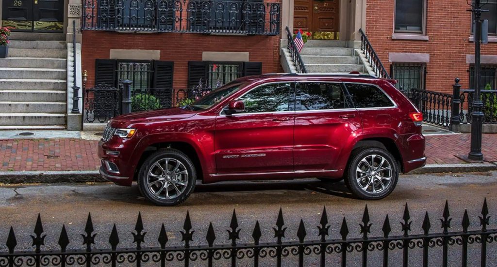 A red Jeep Grand Cherokee SUV is parked outside an apartment house on the street.