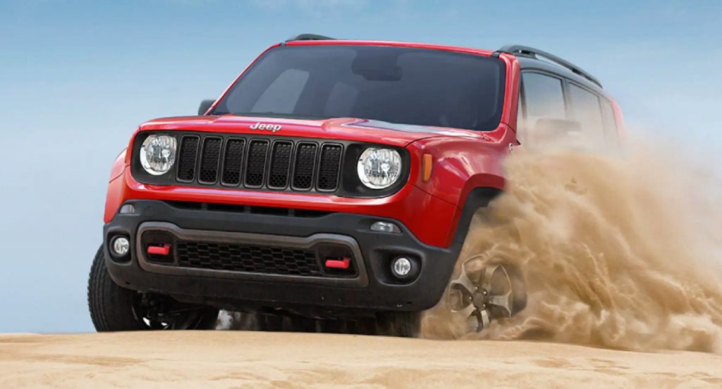 A red 2021 Jeep Renegade Trailhawk off-road SUV is driving through sand.