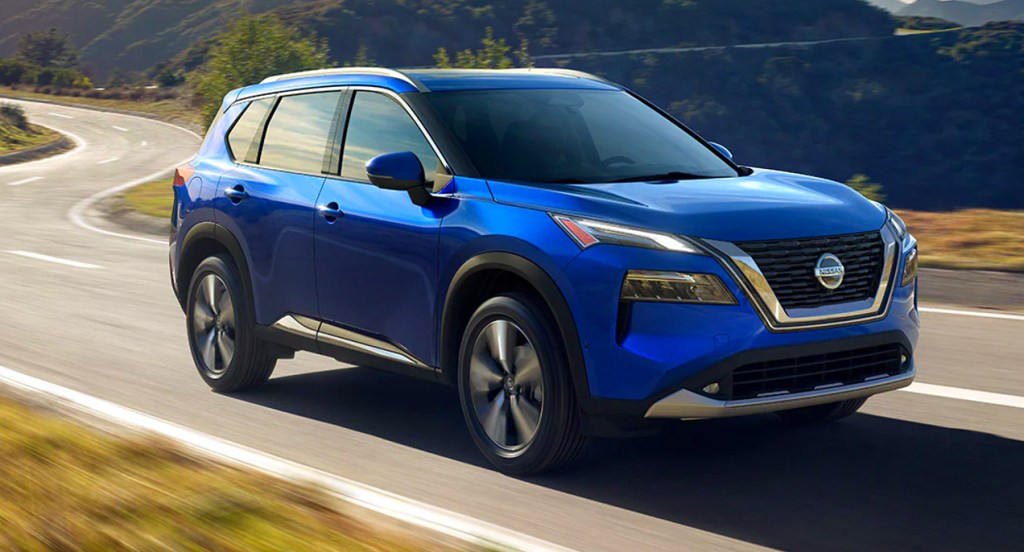 A blue 2021 Nissan Rogue compact SUV is driving on the road. 