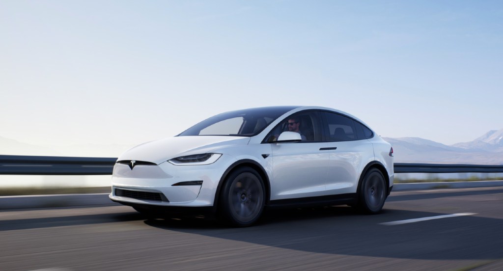 A white Tesla Model X SUV is driving on a highway. 