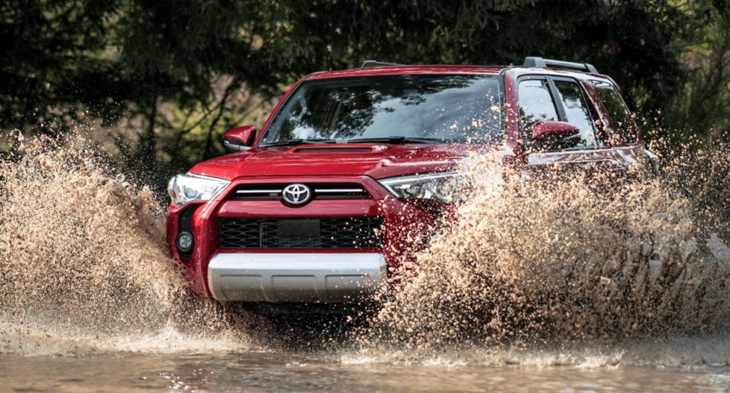 A red Toyota 4Runner SUV is driving through the mud. 