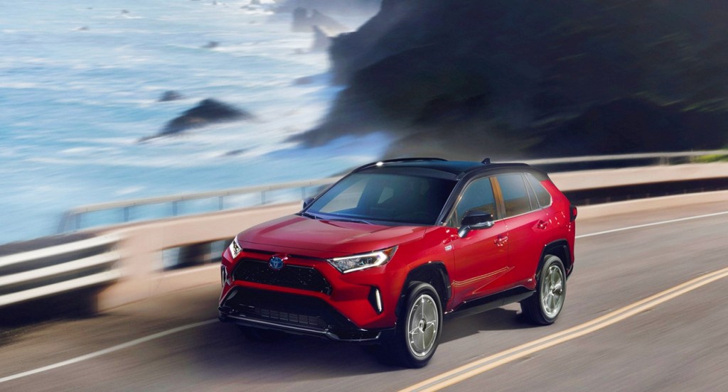 A red Toyota RAV4 Prime is driving on a highway alongside the ocean.