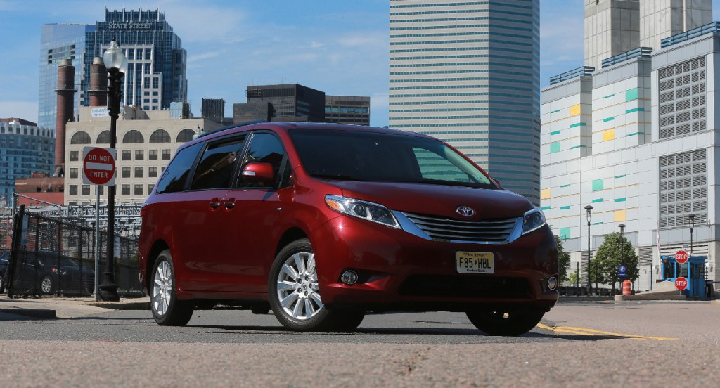 A red Toyota Sienna minivan is parked in the middle of a city street. 