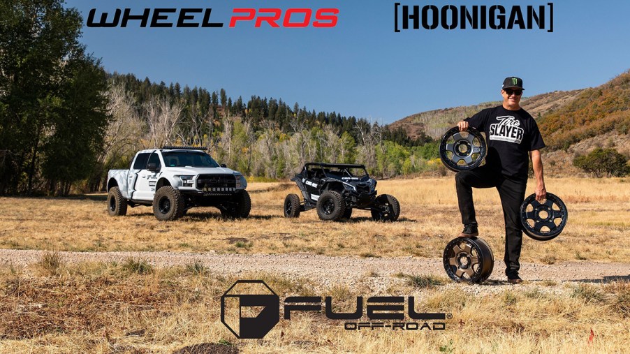 Ken Block's Hoonigan automotive lifestyle brand announces merger with Wheel Pros. Image of Ken Block holding off road wheels in each hand and another wheel under his left foot.
