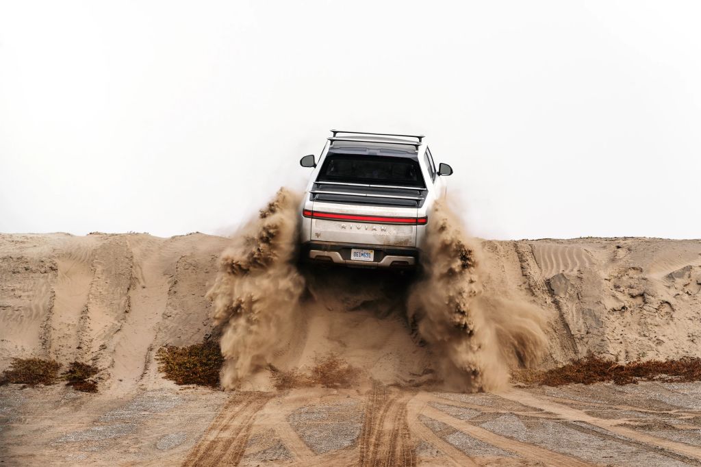 White Rivian R1T driving up a sand dune