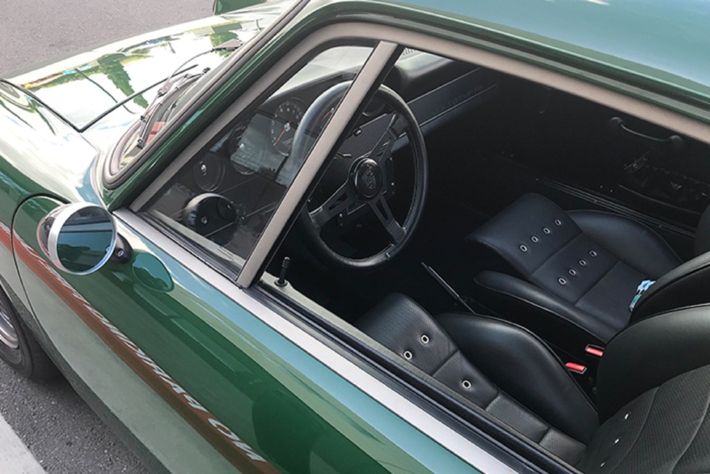 The black-leather-upholstered front seats and black dashboard of Zelectric's green 'Tesla Porsche' 1968 Porsche 912 seen through the driver's side window