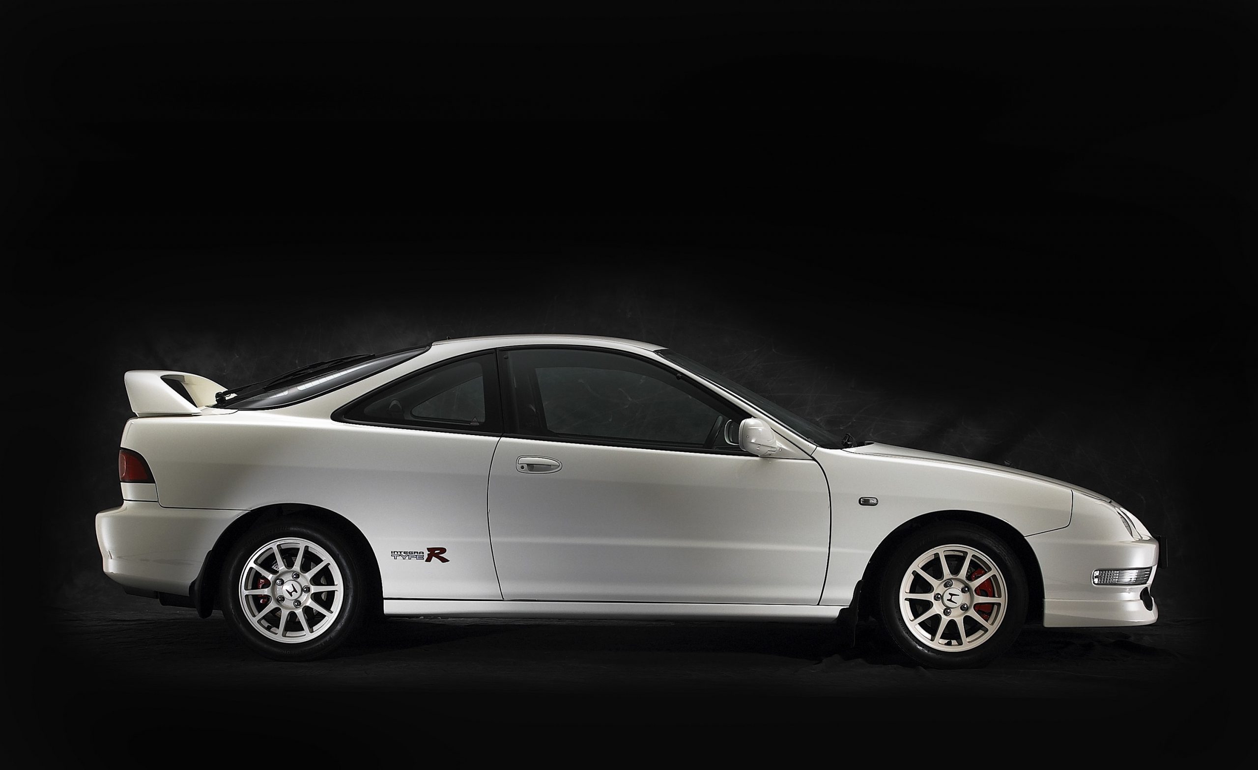 A white Acura Integra Type R shot in profile against a black studio background
