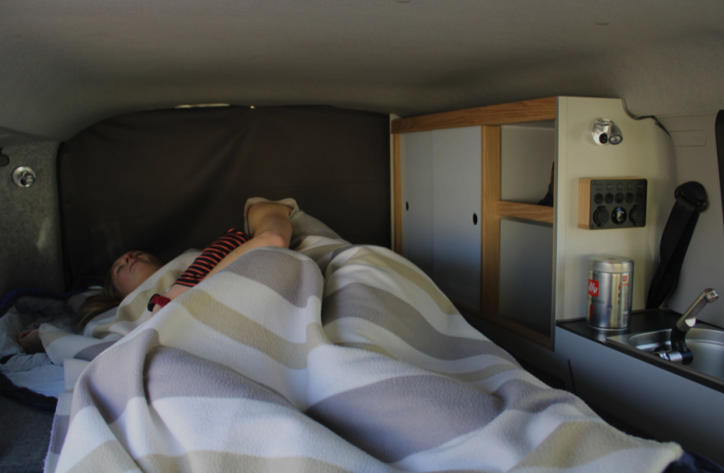 a couples sleeps cozy in the bed of the small camper van