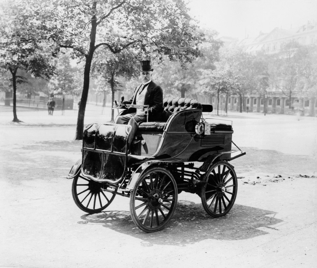 a man in an electric car circa 1899. This car is very similar to the Electric Vehicles Company car that was involved in the first car accident death in America in New York City in 1899.