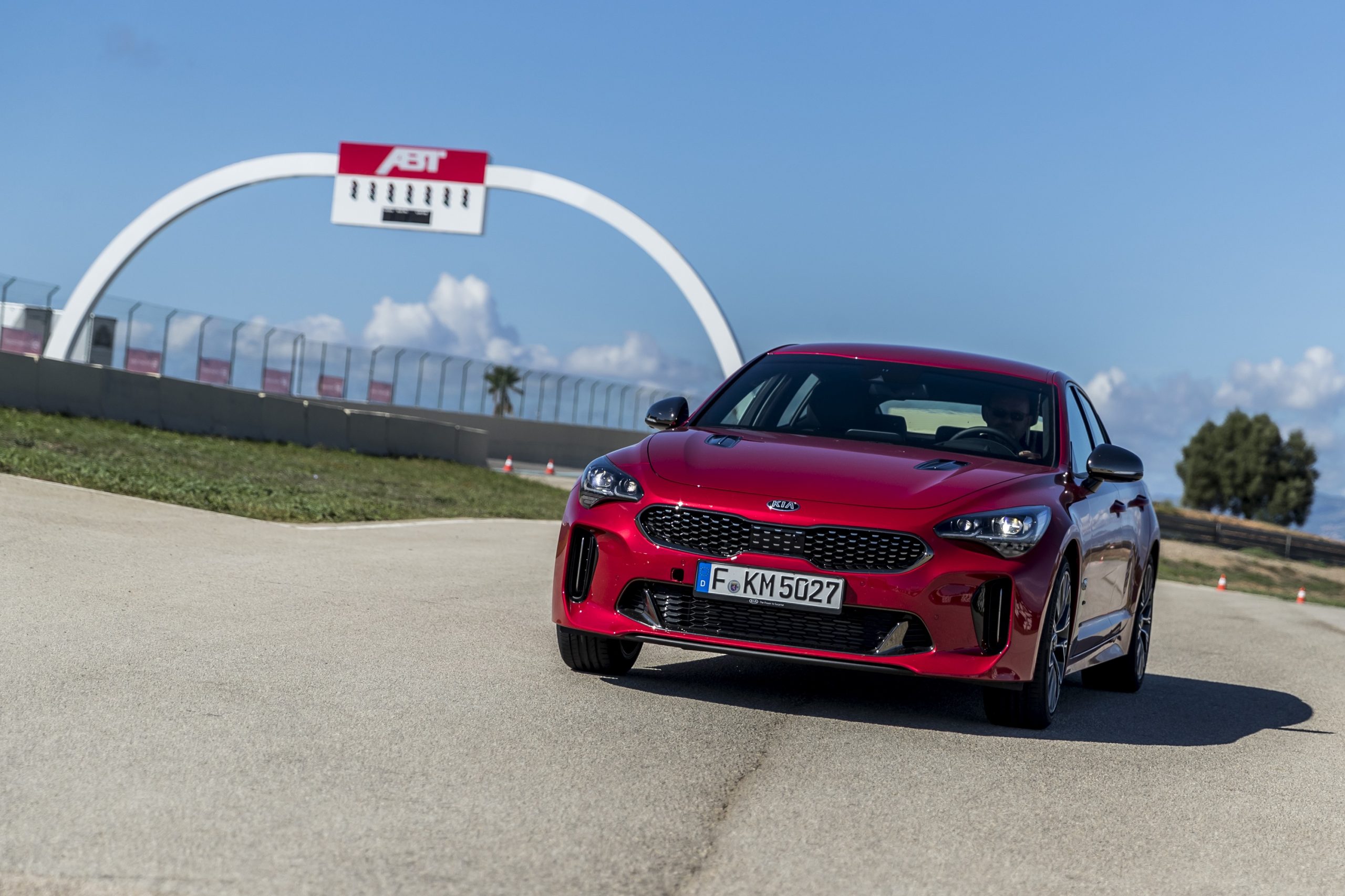 A red Kia Stinger GT on a race track shot from the front 3/4 angle