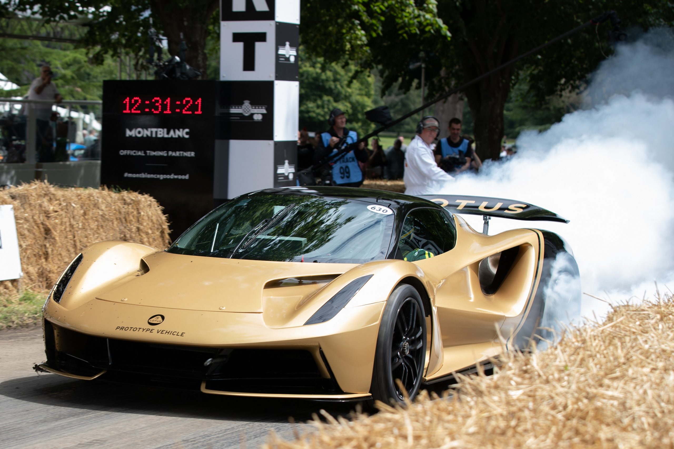 A gold Lotus Evija does a burnout at the start of its lap at the Goodwood Festival of Speed, shot from the front 3/4