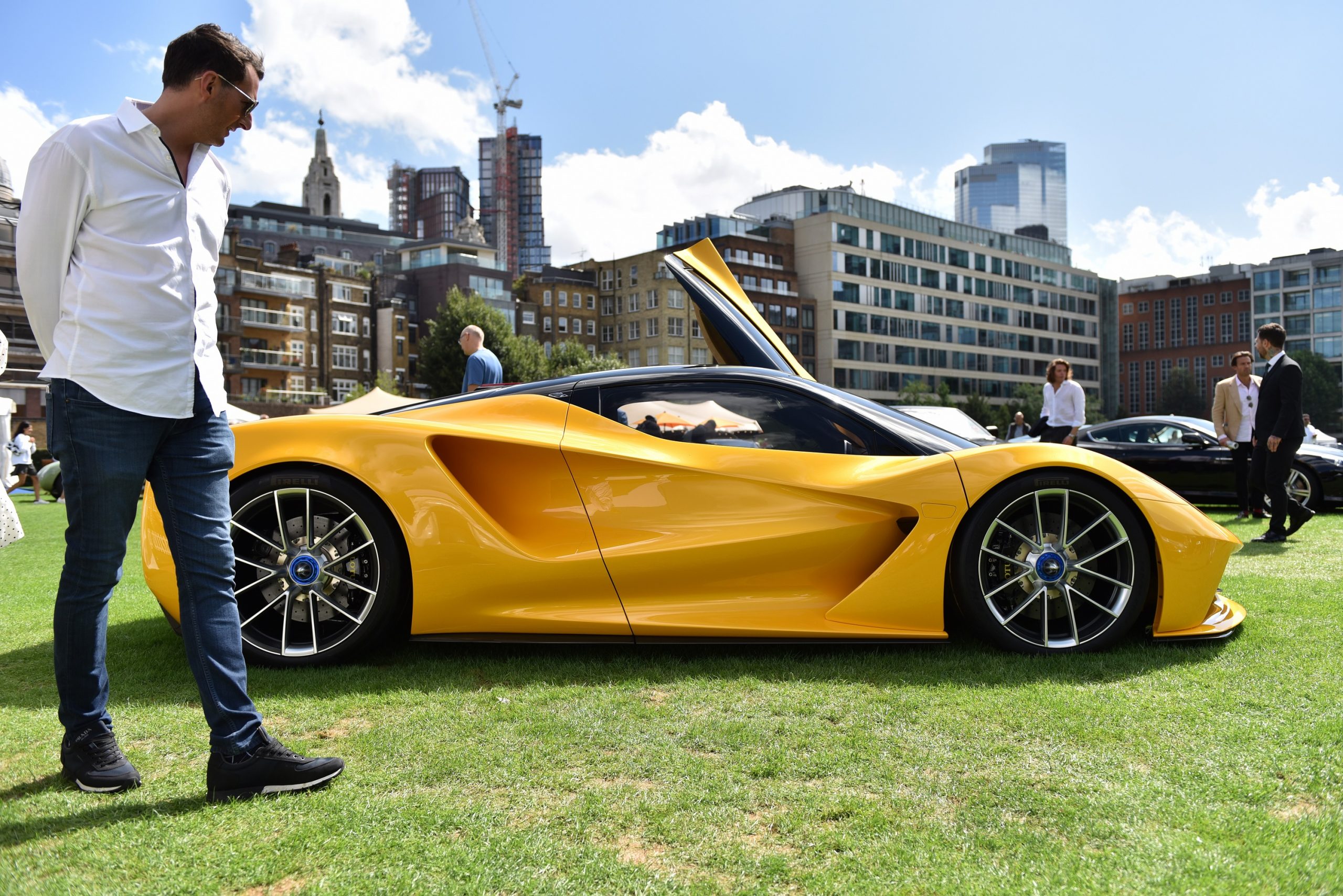 A yellow Lotus Evija is admired by a passerby at a concourse event, shot in profile