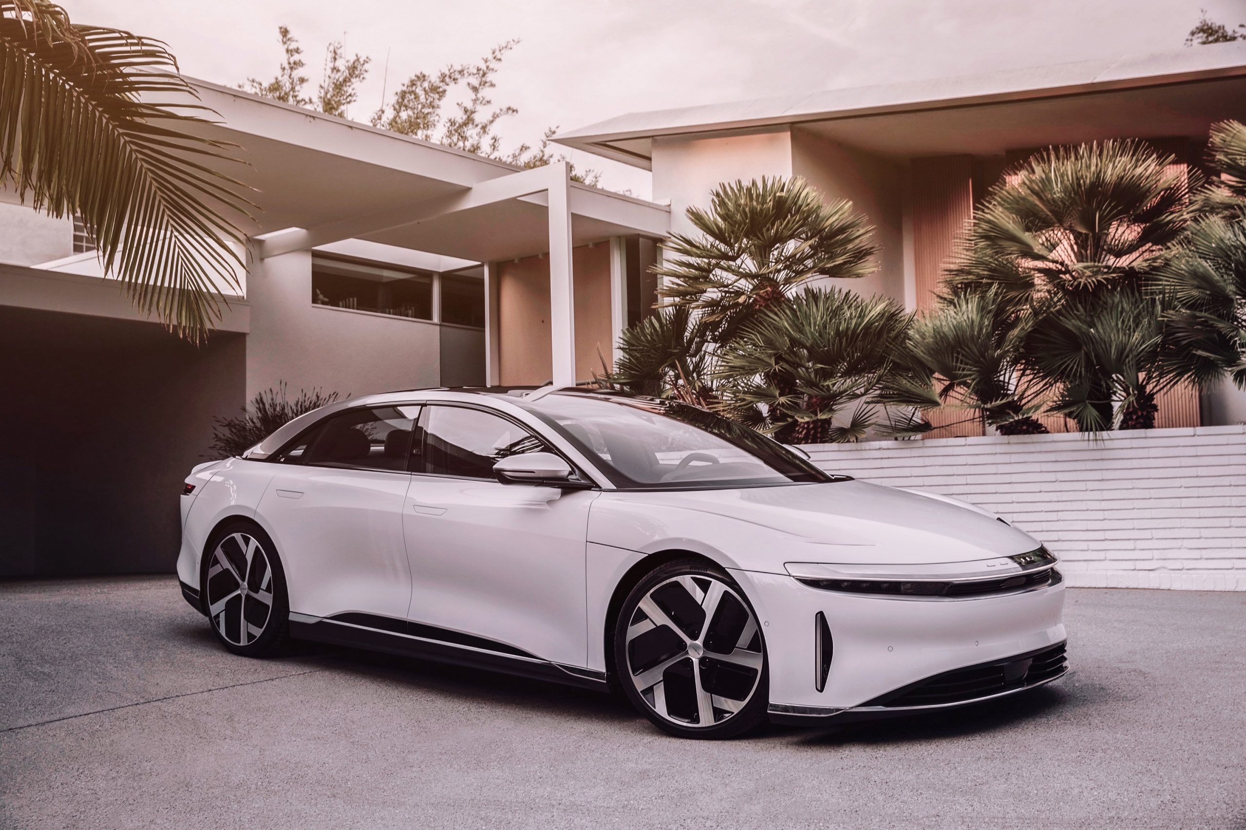 A white Lucid Air luxury EV shot from the front 3/4 angle in a driveway with palms in the background