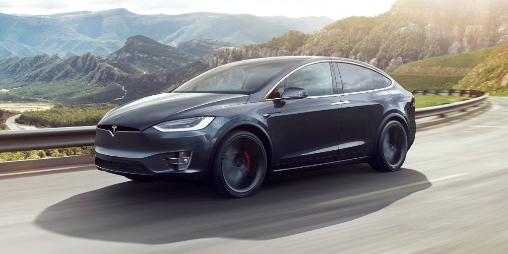 A dark gray Tesla Model X driving past mountains. 