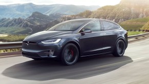 A dark gray Tesla Model X driving past mountains.