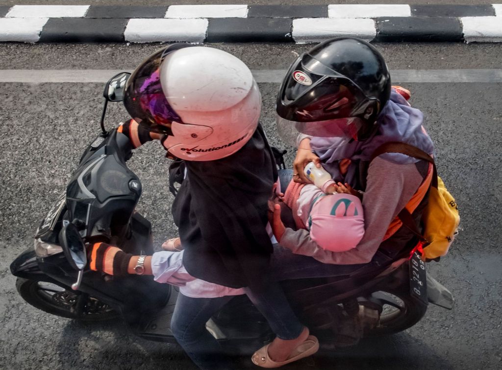 A motorcycle passenger feeds a baby a bottle of milk in Jakarta on August 9, 2017