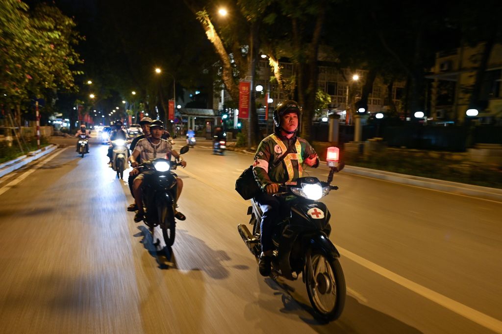 This photograph was taken on May 12, 2020, shows Grab motorcycle rider Pham Quoc Viet (R) riding his motorcycle during a night patrol to help traffic accident victims on the streets of Hanoi. 