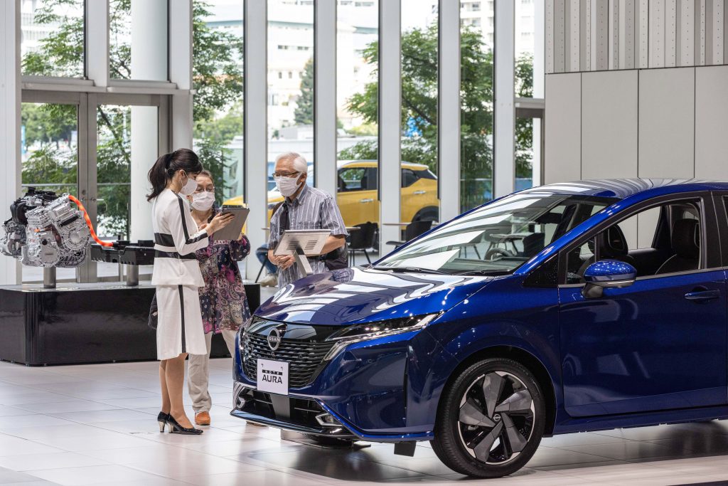 Two reviewers examine a blue Nissan Note.