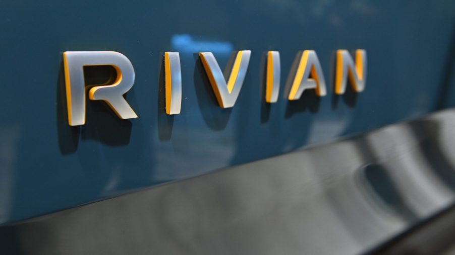 A grey Rivian logo on the back of a blue R1T truck at an auto show
