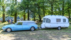 A station wagon towing an RV camper in a forest campground