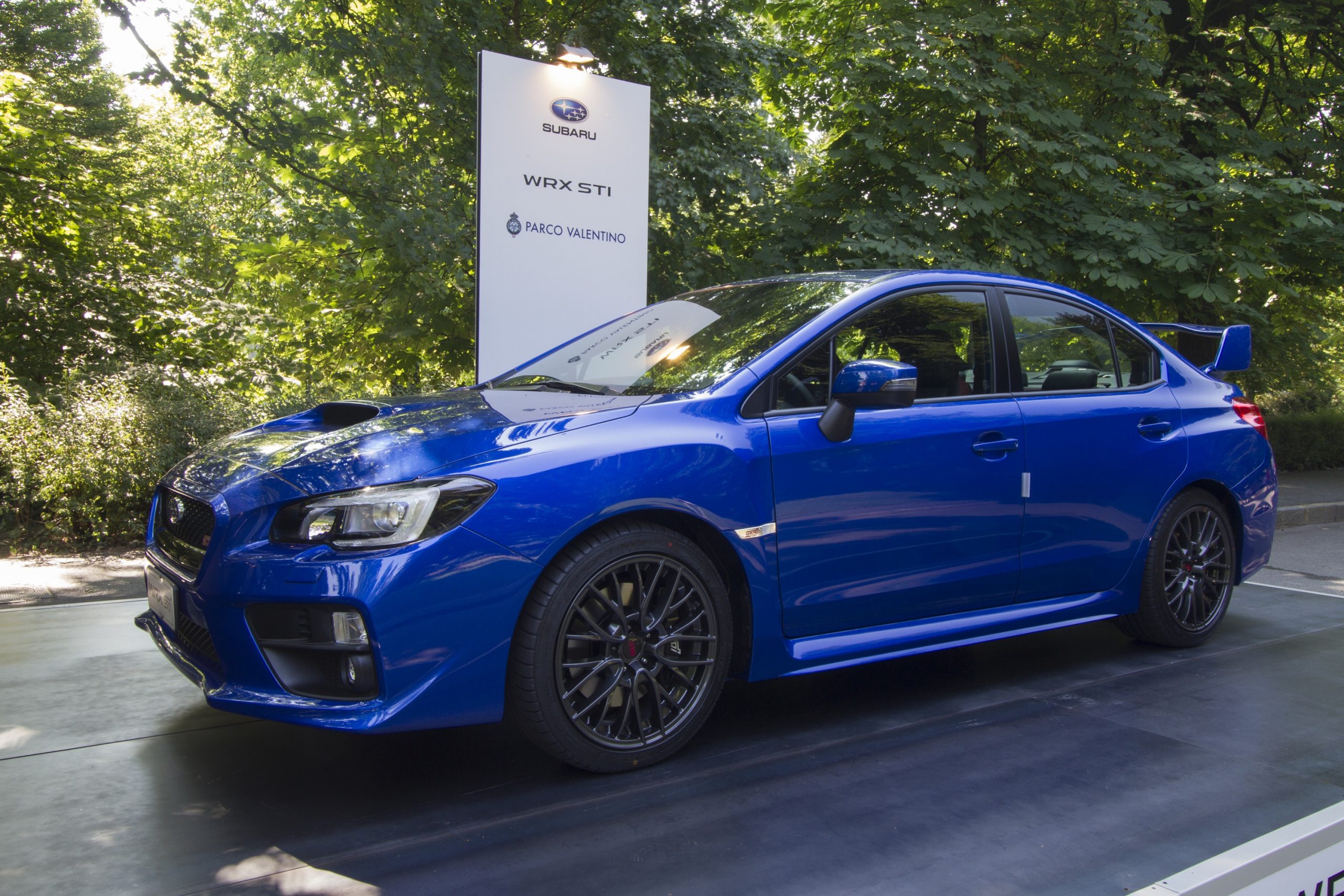 A blue 2021 Subaru WRX STI at an auto show shot under the trees from the front 3/4