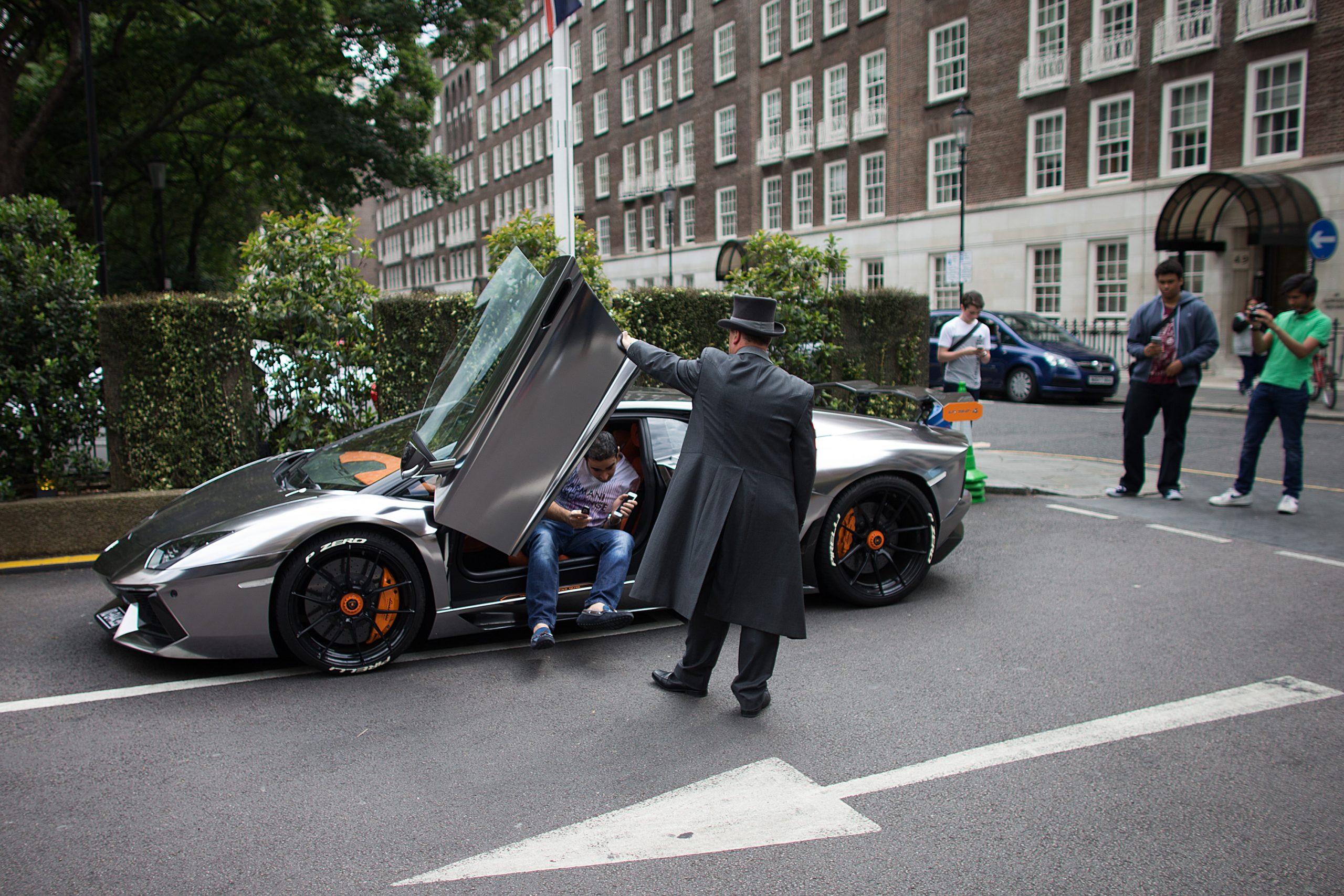A valet helps an owner out of his silver Lamborghini supercar