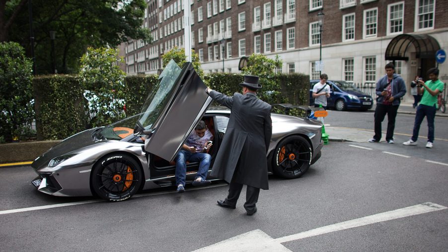 A valet helps an owner out of his silver Lamborghini supercar