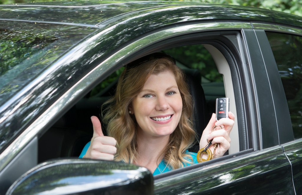 A teen driving a car gives a thumbs-up