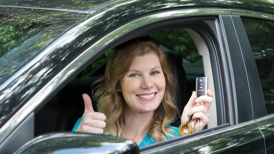 A teen driving a car gives a thumbs-up