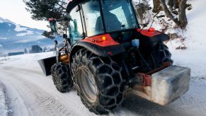 A tractor driving on a snowy road with with snow chains on its tires