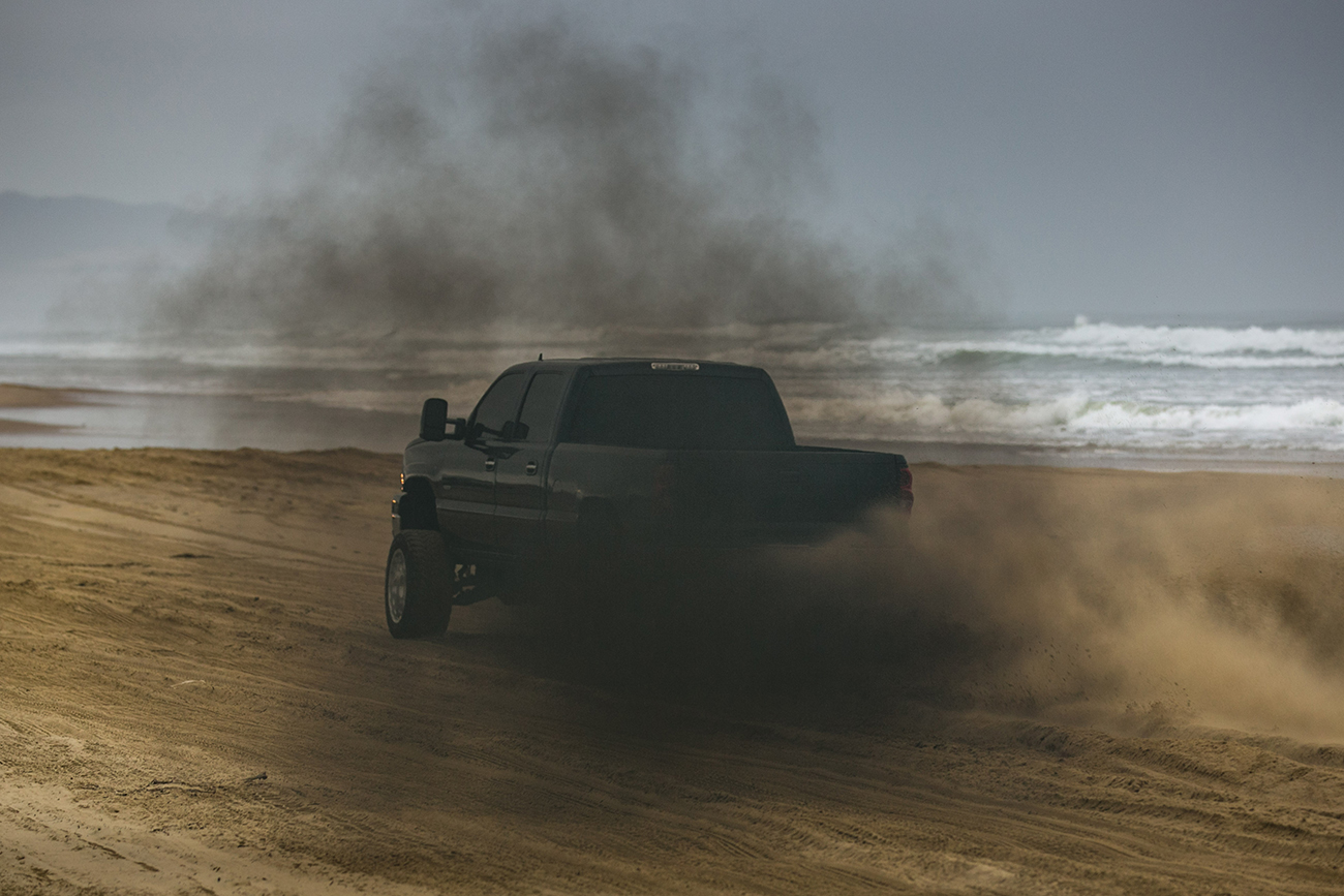 A black truck rolling coal on a beach.