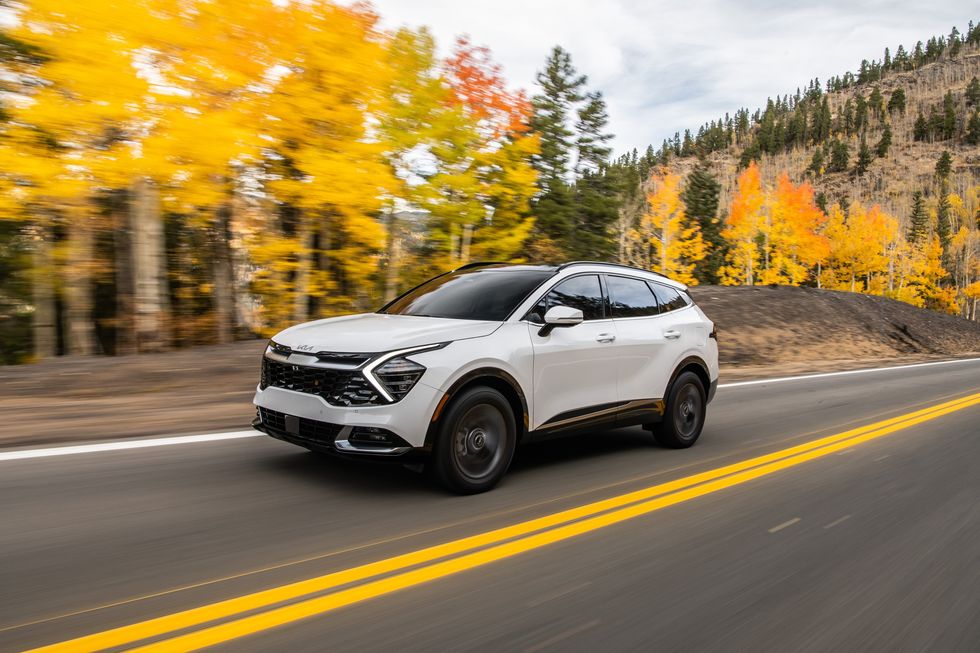 A white 2023 Kia Sportage driving through fall scenery during the day