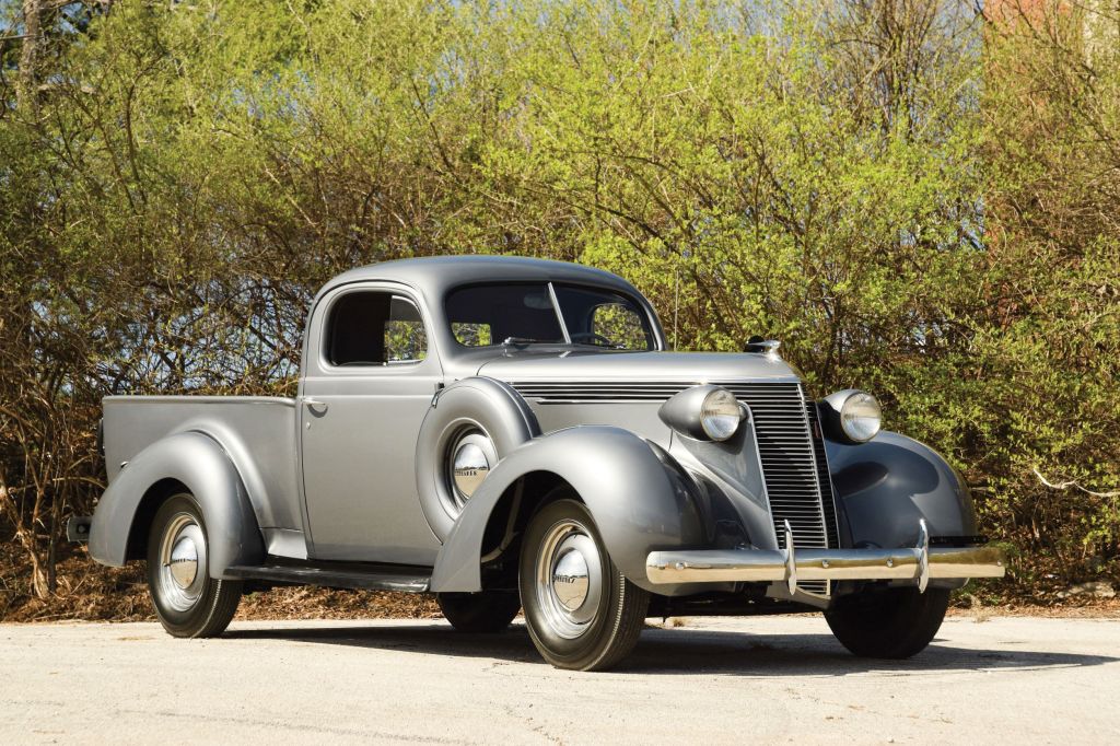 A gray 1937 Studebaker J5 Coupe Express parked by a green hedge