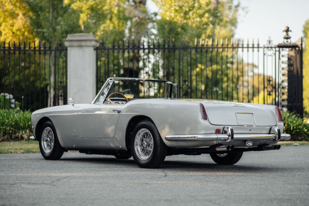 The rear 3/4 view of a white 1961 Ferrari 250 GT Pinin Farina Cabriolet Series II parked inside a gated lawn
